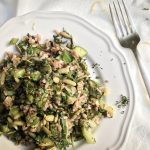 wild rice salad with mint and preserved lemon piled on a white plate with a silver fork next to it.