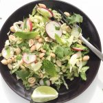 Thai salad with radish, mint and peanuts on a dark plate with a slice of lime and a fork